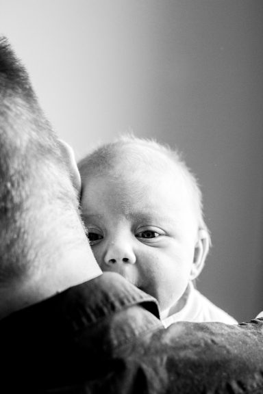 Een baby kijkt over de schouder van een volwassene, in zwart-wit.
